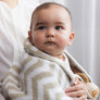 A cute baby wrapped snugly in a soft, cozy Taupe Chevron Knitted Chenille Blanket while being held.