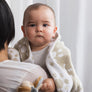 Smiling baby wrapped in a soft Taupe Sunflower Knitted Chenille Blanket while being held by their mother.