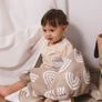 A toddler sitting up comfortably, partially covered by the Taupe Rainbow Knitted Chenille Blanket, for a close-up lifestyle view.