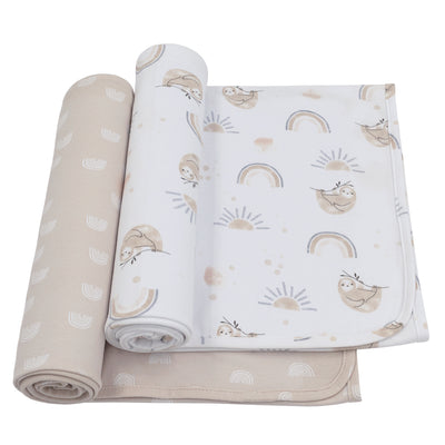 Front studio view of a 2-pack cotton jersey baby swaddle blanket set, featuring one blanket rolled in a solid beige arch pattern and the other partially unrolled to showcase a watercolor print of sleeping sloths, boho rainbows, and suns.