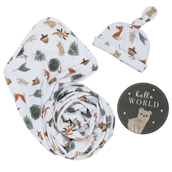 Hello World 3-piece newborn gift set in Forest Retreat style, featuring a soft white jersey cotton swaddle blanket and matching printed top-knot baby beanie with watercolor foxes, bears, and pine trees, alongside a round milestone disc.