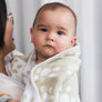 A close-up profile shot of a mother holding her baby wrapped snugly in a cozy Taupe Sunflower Knitted Chenille Blanket.