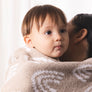 A young child snuggled and held up while wearing the cozy Knitted Chenille Blanket, highlighting its softness.