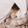 Candid photo of a toddler playfully covered by the Knitted Chenille Blanket, with the blanket draped over their head like a canopy, showing the rainbow pattern.