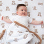Happy infant lying flat on a matching teddy bear printed sheet, partially covered with the cozy Cuddly Bear sherpa fleece blanket.