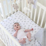 High angle view of a baby lying in a white wooden crib looking up at the hanging plush toys of the Elephant Heritage Musical Mobile.