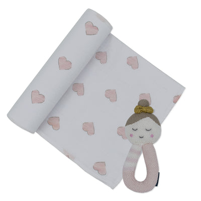 Product shot of the baby gift set featuring a white cotton muslin swaddle blanket printed with soft pink hearts, partially unrolled next to the coordinating 