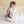 Nursery lifestyle view of a baby sitting up on a bed wrapped in a white blanket, holding the Charley Fox knitted ring rattle.