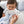 Nursery lifestyle view of a smiling baby boy holding the soft Theodore Elephant knitted ring rattle while cuddled with a light blue plush blanket on a grey couch.
