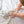 Close-up nursery lifestyle view of a baby's hands reaching out and gripping the soft Finn Giraffe knitted ring rattle on a white fabric surface.