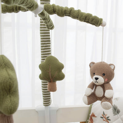 Close-up view of the Forest Retreat musical crib mobile, highlighting a soft knitted brown bear and a green felt tree hanging from a fabric-covered olive green and white striped arm.