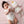Overhead nursery lifestyle view of a newborn baby lying on a pink blanket, cradling the Kenzie Unicorn ring rattle next to a matching large unicorn knitted plush toy.
