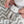Close-up nursery lifestyle view of a baby's hands holding the soft Austin Lion knitted ring rattle, resting next to a white and grey chevron-patterned baby blanket.