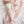Close-up nursery lifestyle view showing the Amy Mermaid knitted ring rattle lying next to a matching large mermaid knitted plush toy on a pink and white heart-patterned muslin swaddle blanket.