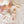 Close-up overhead lifestyle view of a baby sitting next to a collection of animal-shaped knitted ring rattles, including the unicorn, a cat, and a monkey, laid out on a heart-patterned muslin swaddle blanket.