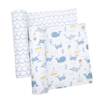 Studio flat lay shot of the two cotton muslin swaddle blankets, showing the wave pattern swaddle rolled up tightly and the whale print blanket partially unfolded to reveal its full detailed pattern.